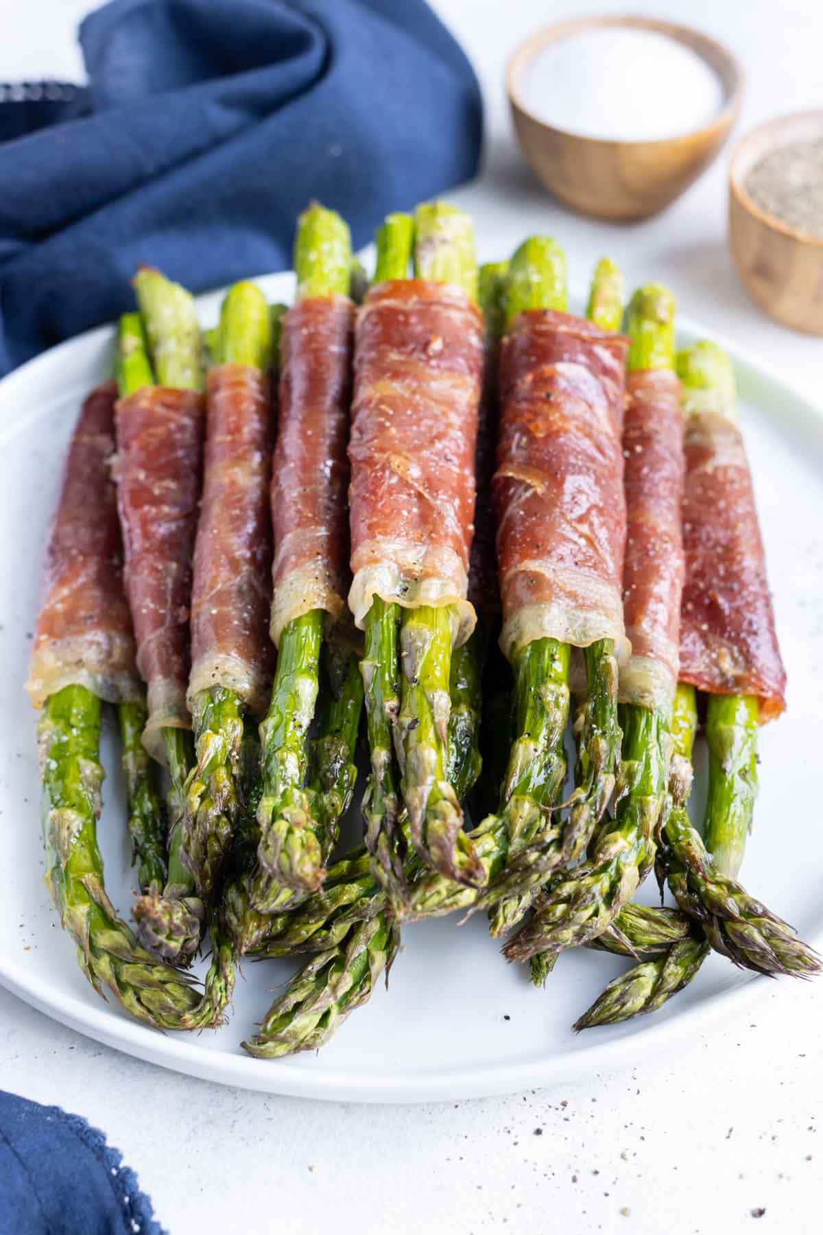 Bundles of prosciutto-wrapped asparagus are served on a white plate.