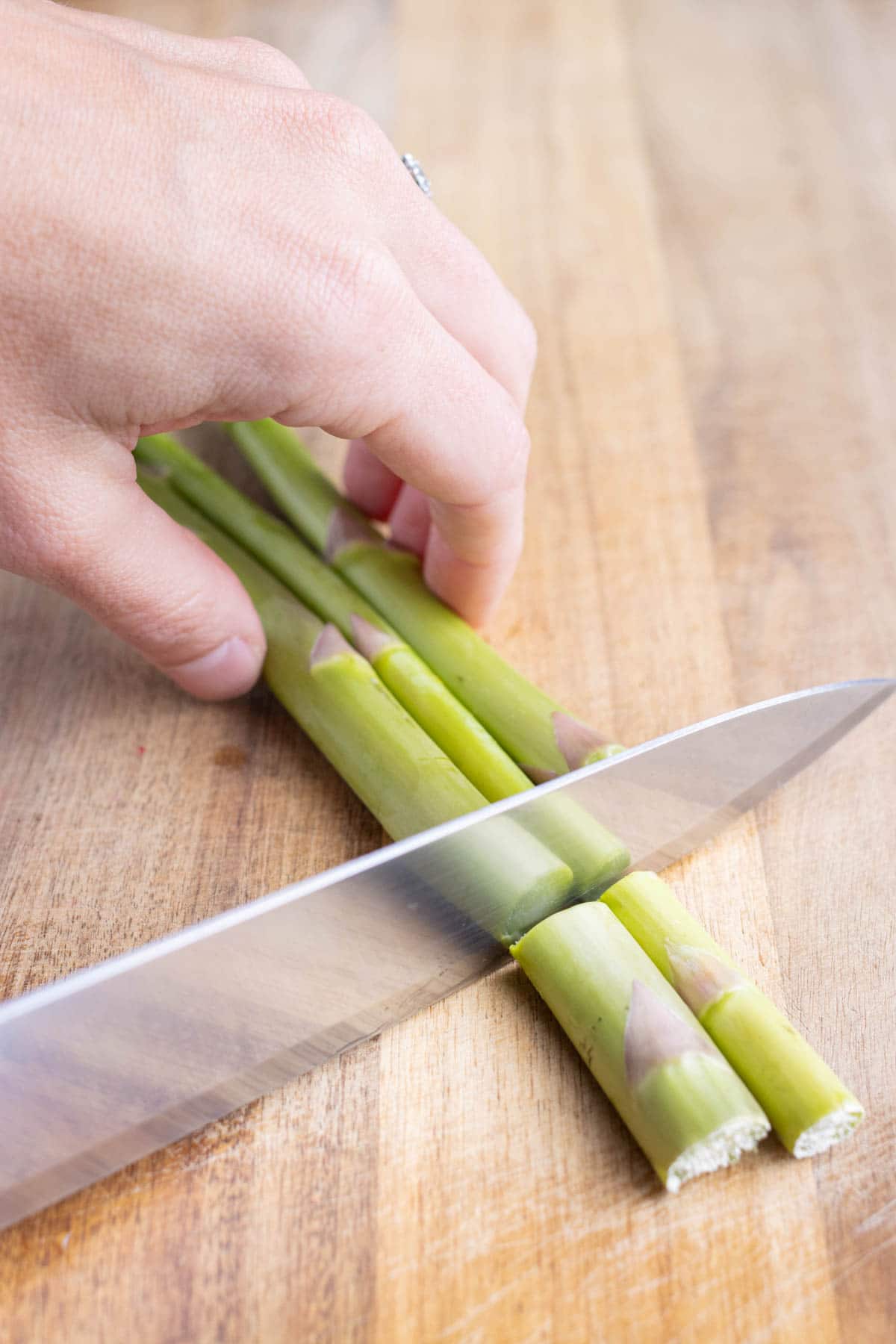 A knife is used to cut the ends of the raw asparagus.