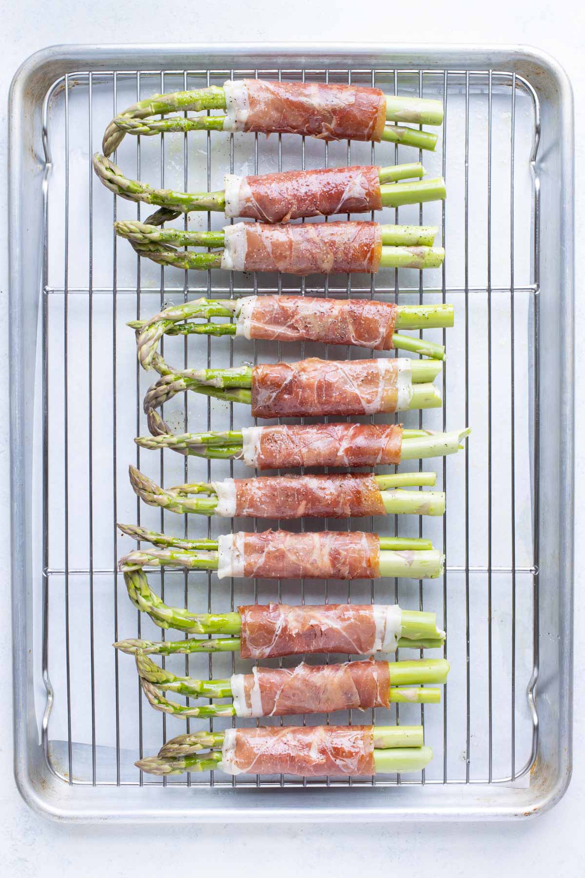 Asparagus wrapped in prosciutto is baked in the oven in one layer.