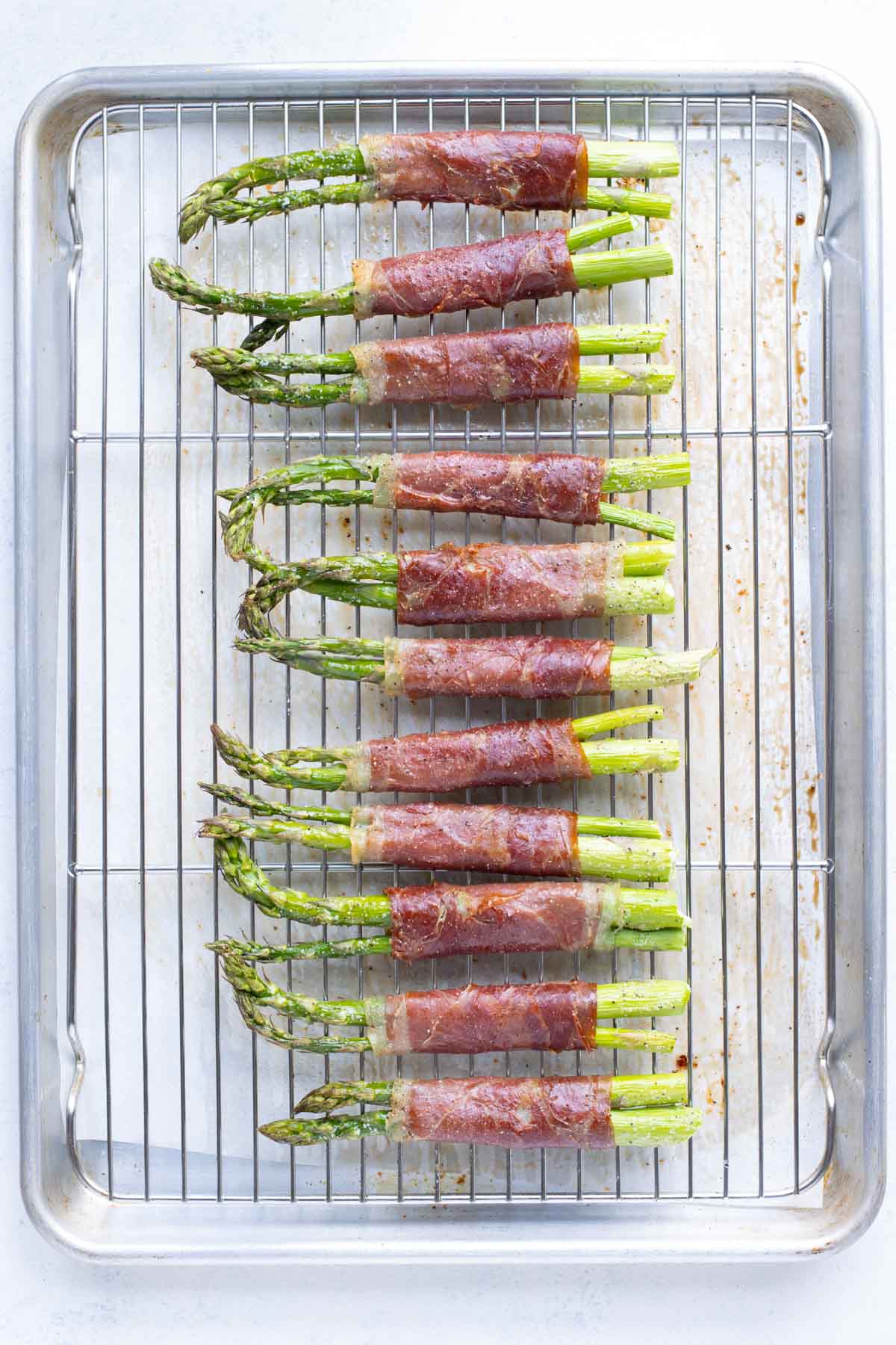Tender asparagus and crisp prosciutto is cooked on a baking sheet in the oven.
