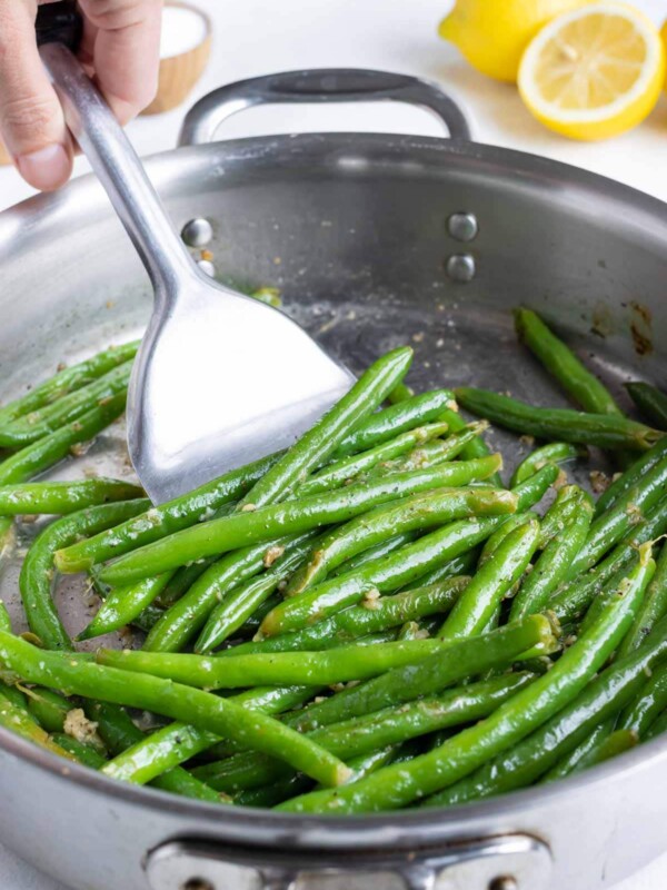 Tender green beans are removed from the skillet with a spatula.