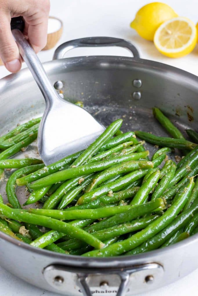 Tender green beans are removed from the skillet with a spatula.