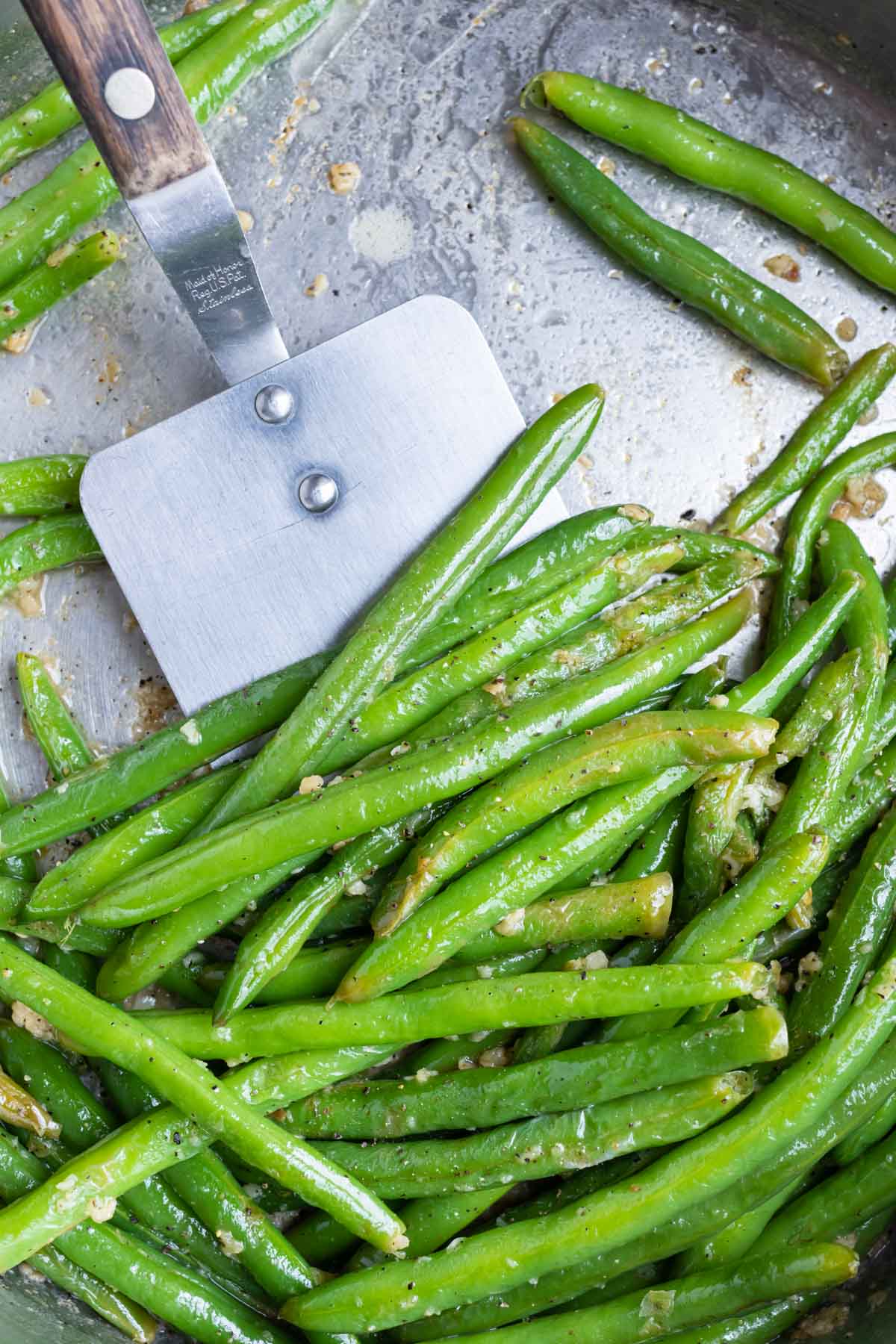A spatula is used to remove the green beans from the skillet.