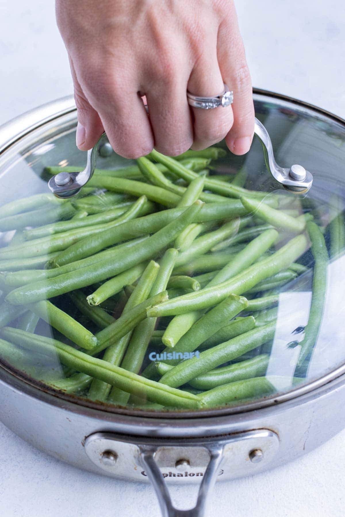 Fresh green beans are boiled on the stove with the lid on the pot.