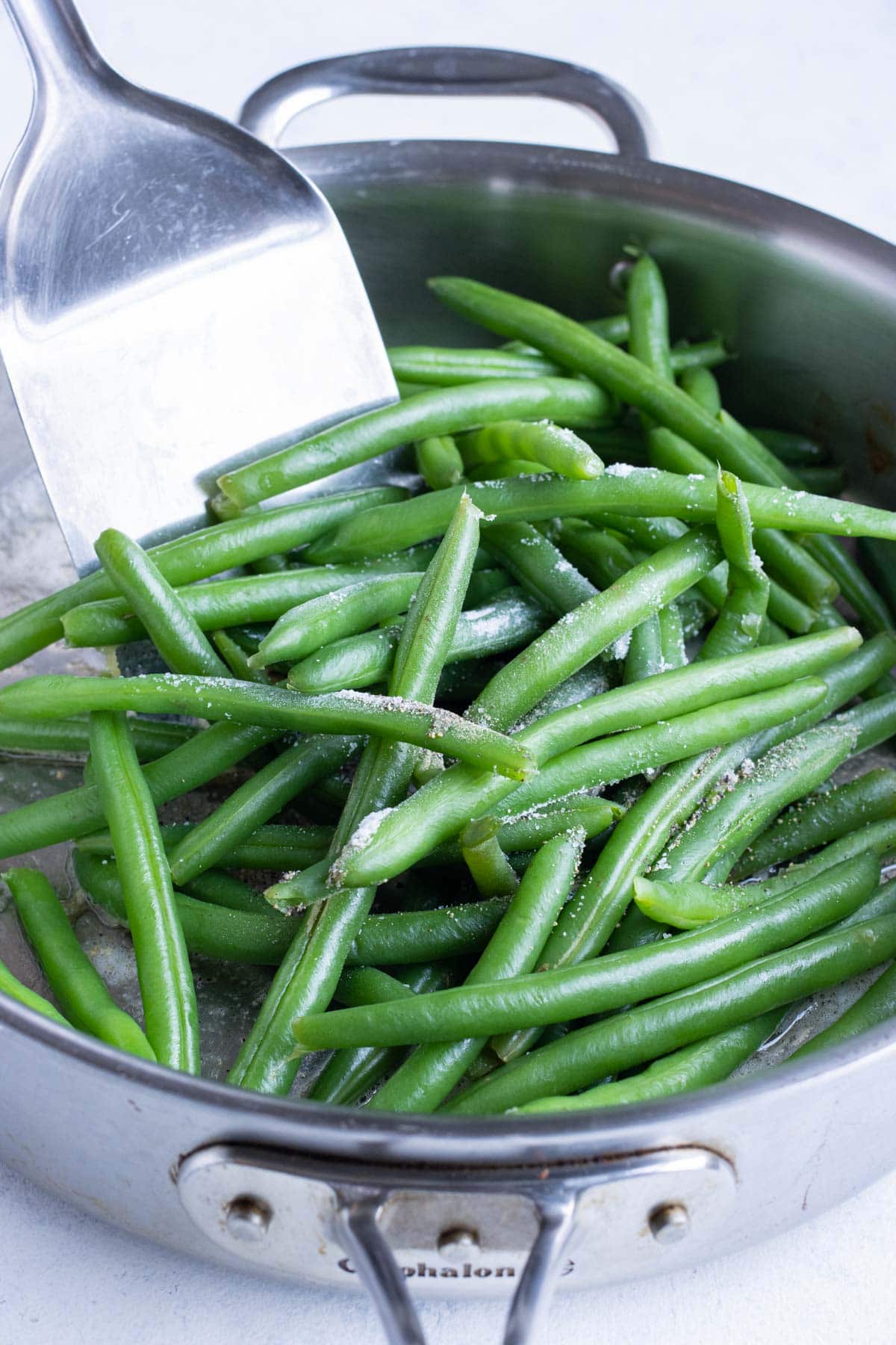 Boiled green beans are added to the garlic butter on the stove.
