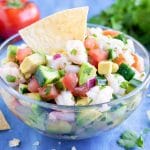 A clear bowl full of an easy shrimp ceviche recipe with a tortilla chip in it.