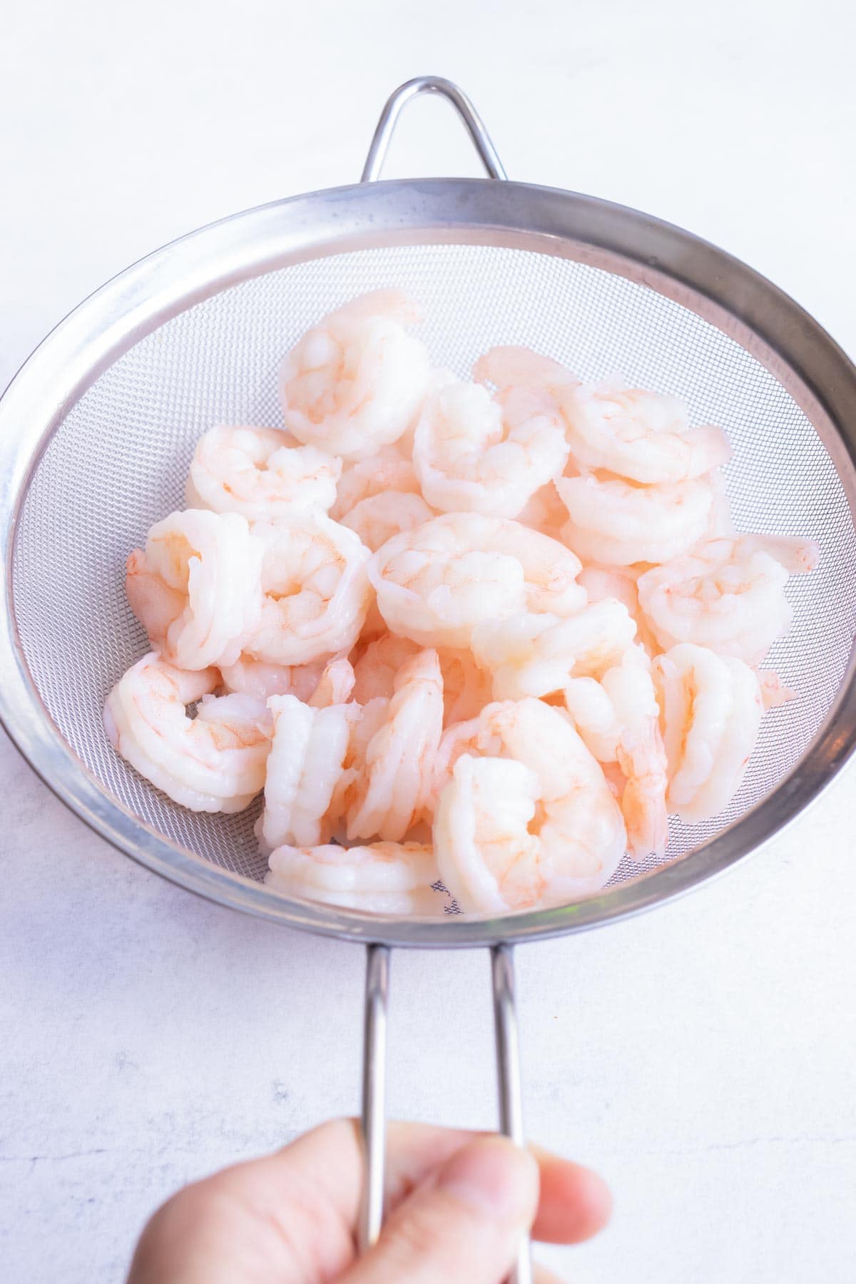 Pre-boiled pink shrimp drained in a small strainer.