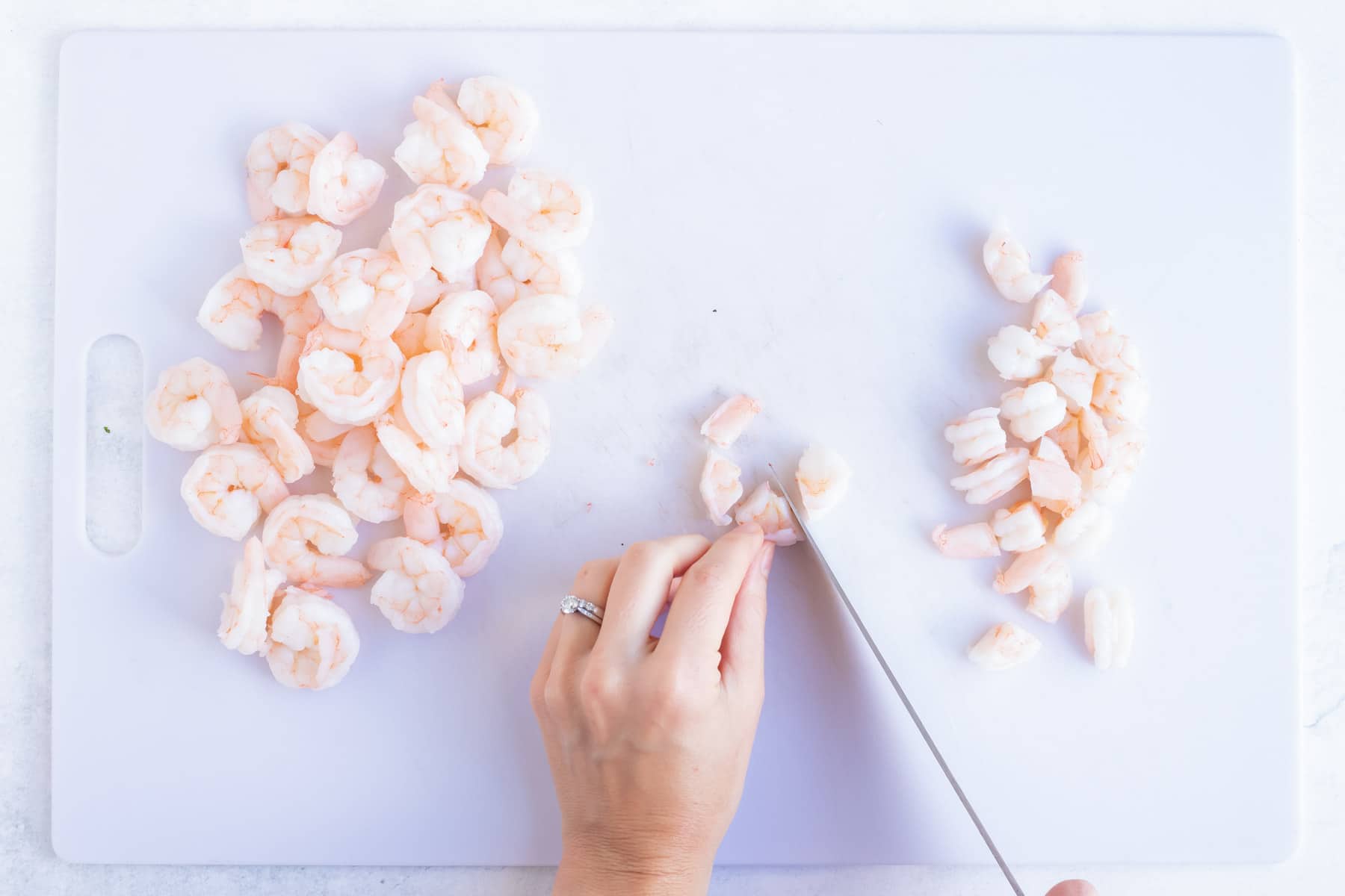 Pink shrimp on a cutting board being chopped into bite-sized pieces.