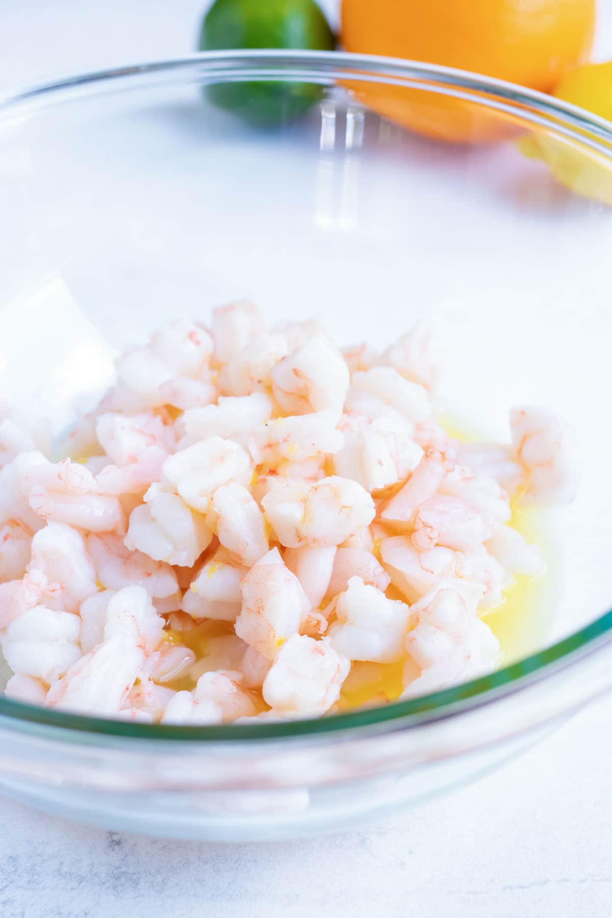 Chopped pink shrimp sits in a glass bowl of citrus marinade.