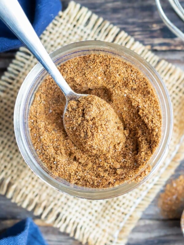 Homemade taco seasoning recipe in a glass container with a silver spoon scooping some out.