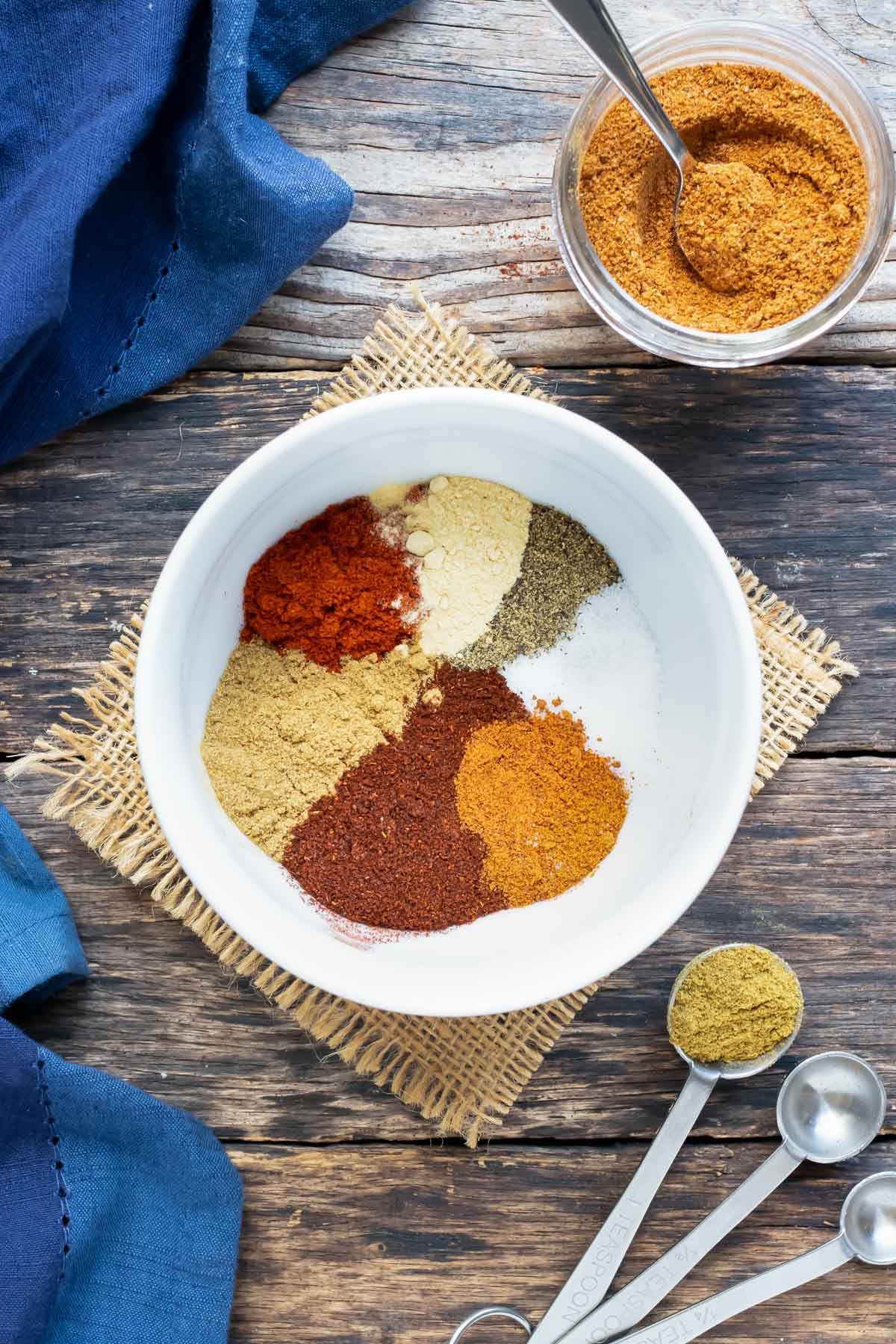 Cumin, paprika, cayenne pepper, garlic powder, chili powder, salt, and pepper, in a white bowl as the ingredients in a homemade taco seasoning recipe.