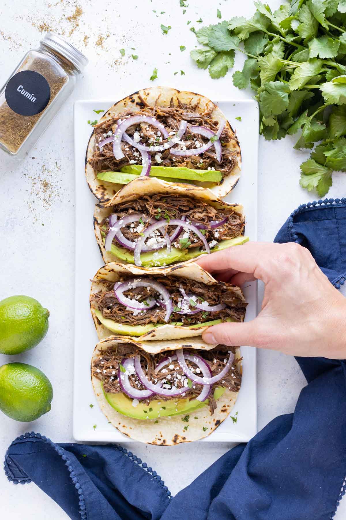 A hand is shown taking a taco from the plate.