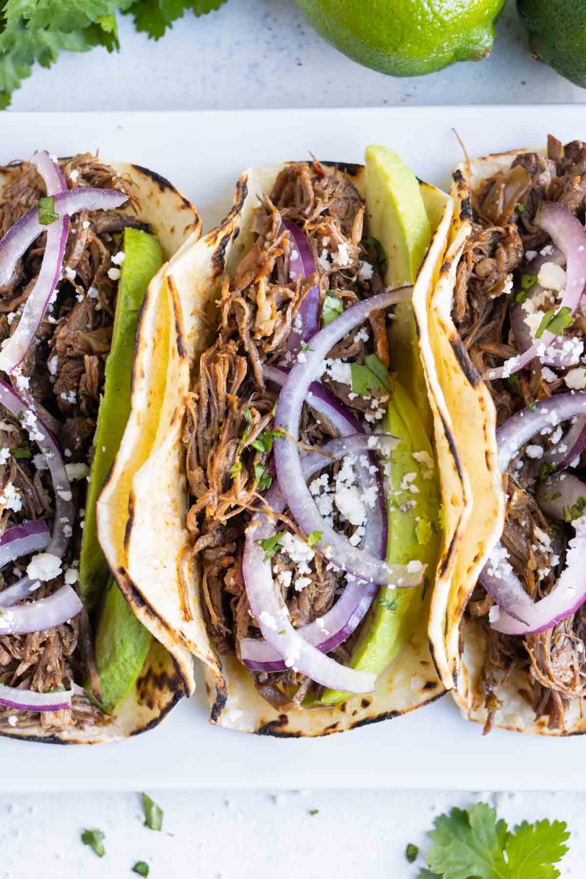 Tacos are loaded with beef barbacoa and served with red onion and cilantro.