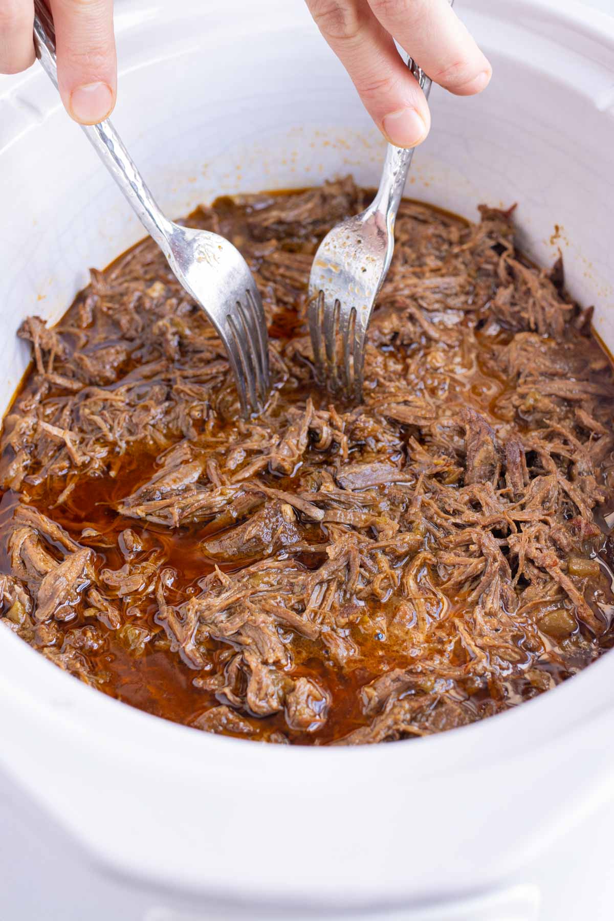 Forks are used to shred beef in the slow cooker.