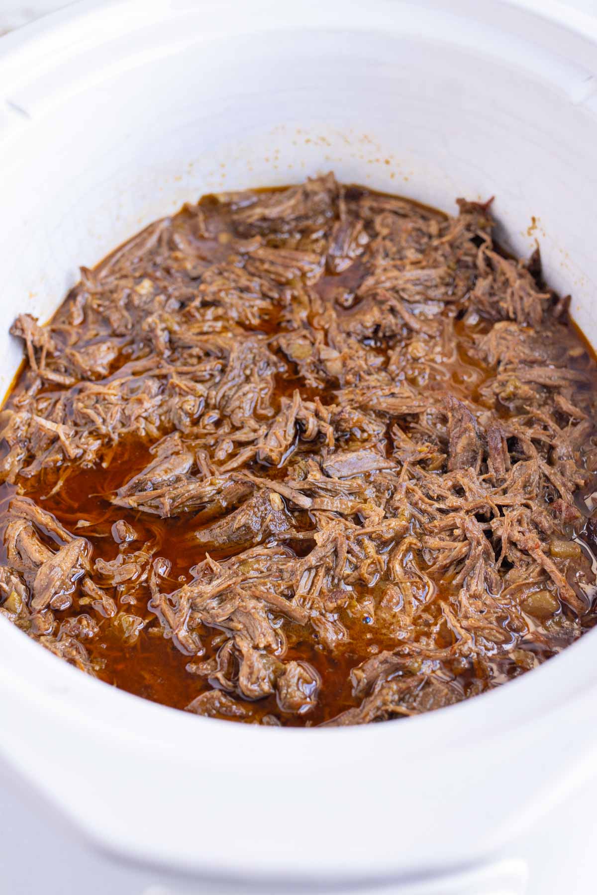 Shredded beef barbacoa is shown in the slow cooker before adding to tacos.