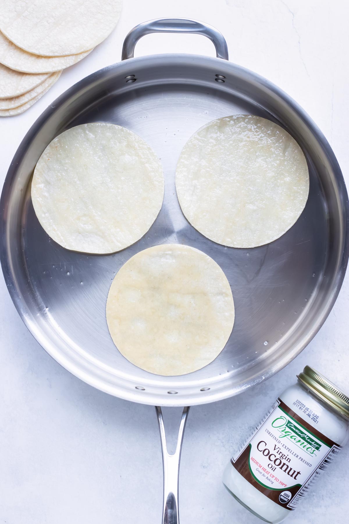 Heating up corn tortillas in a skillet with oil to make them pliable to roll up easily.