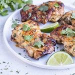Chicken thighs are plated and topped with fresh cilantro and lime juice.