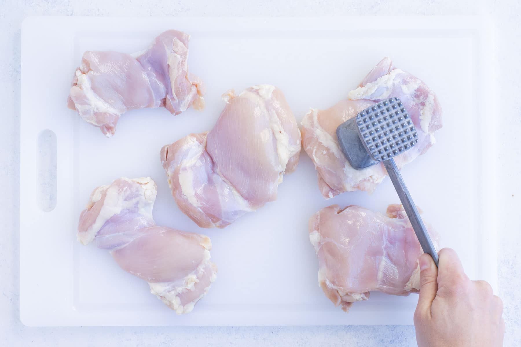 Chicken thighs are pounded until thickness is even.