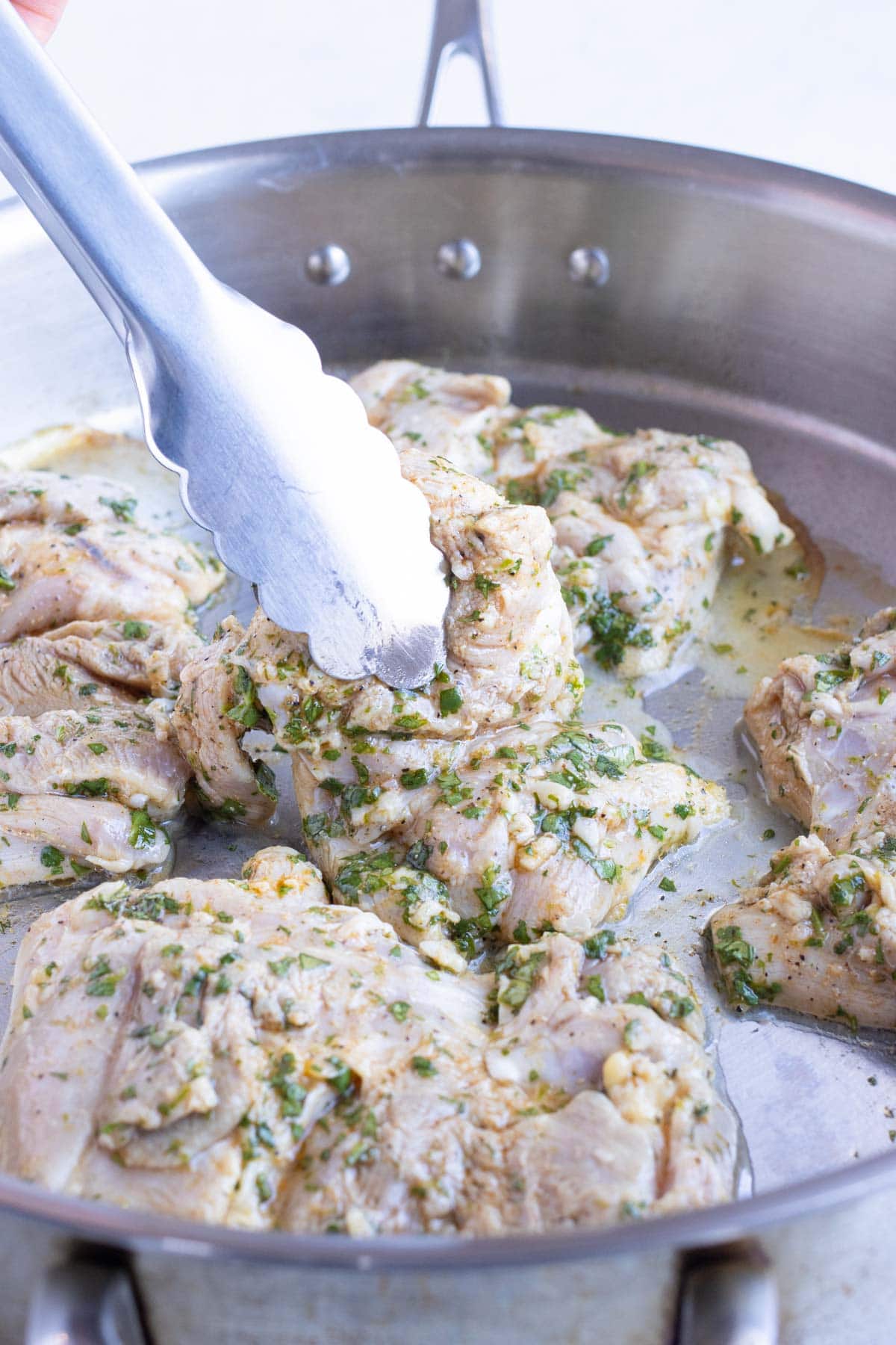 Prepared chicken thighs are cooked in a skillet with oil.