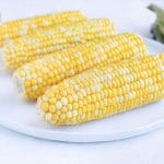 Four ears of corn are served on a plate for a side dish.