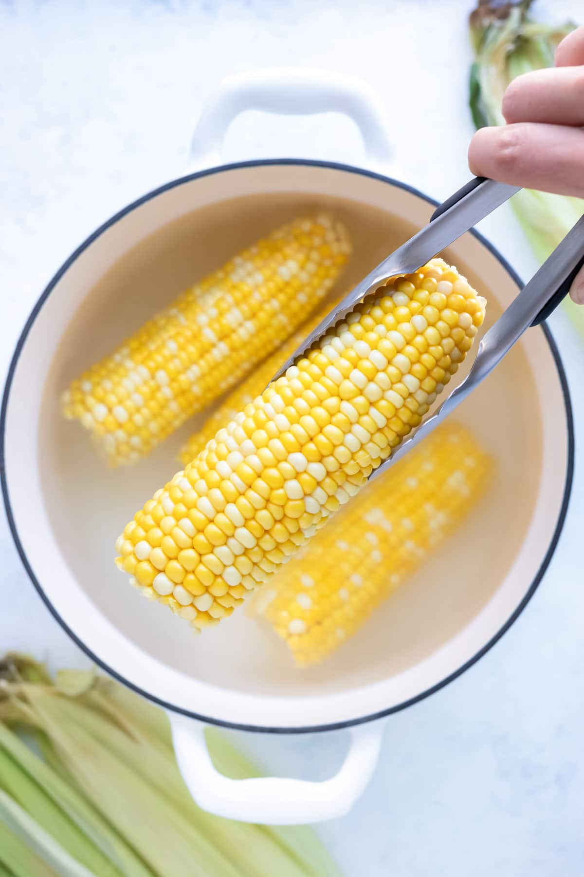 Tongs are used to remove the corn from the water.