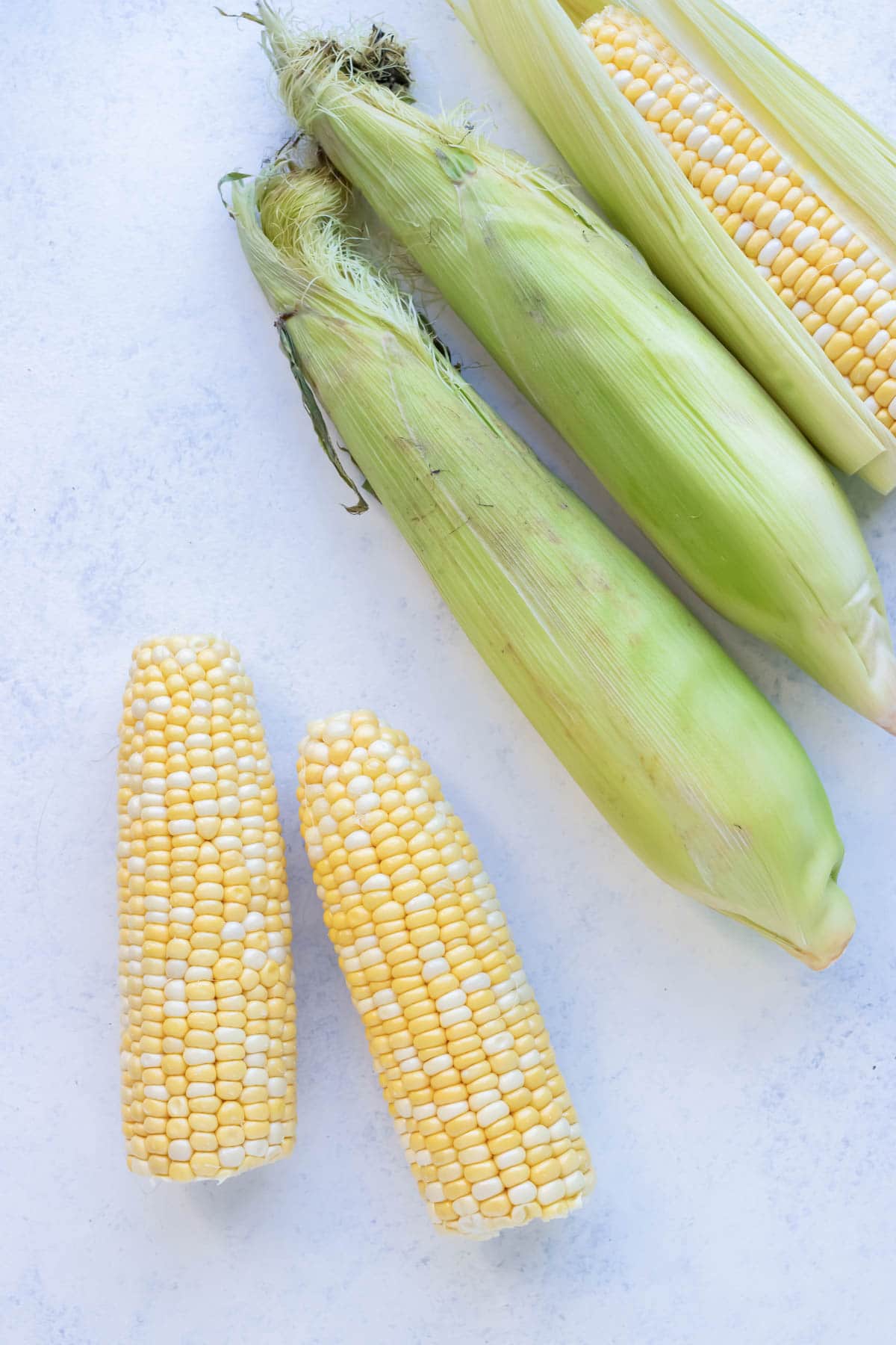 Corn with and without husks are shown on the counter.