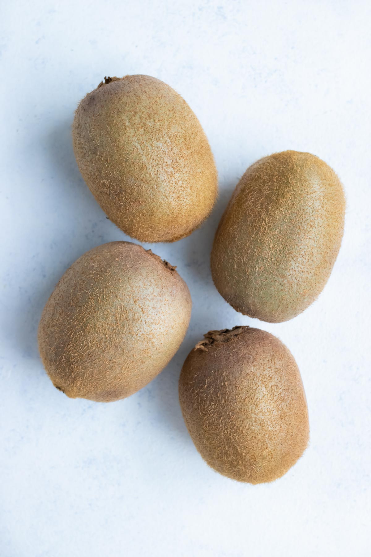 Four kiwi with skins are placed on the counter.