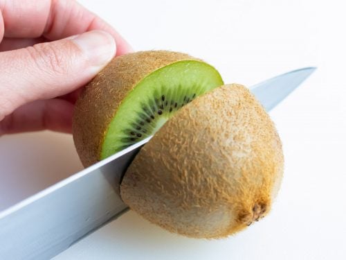 The kiwi is cut in half with a knife before peeling.