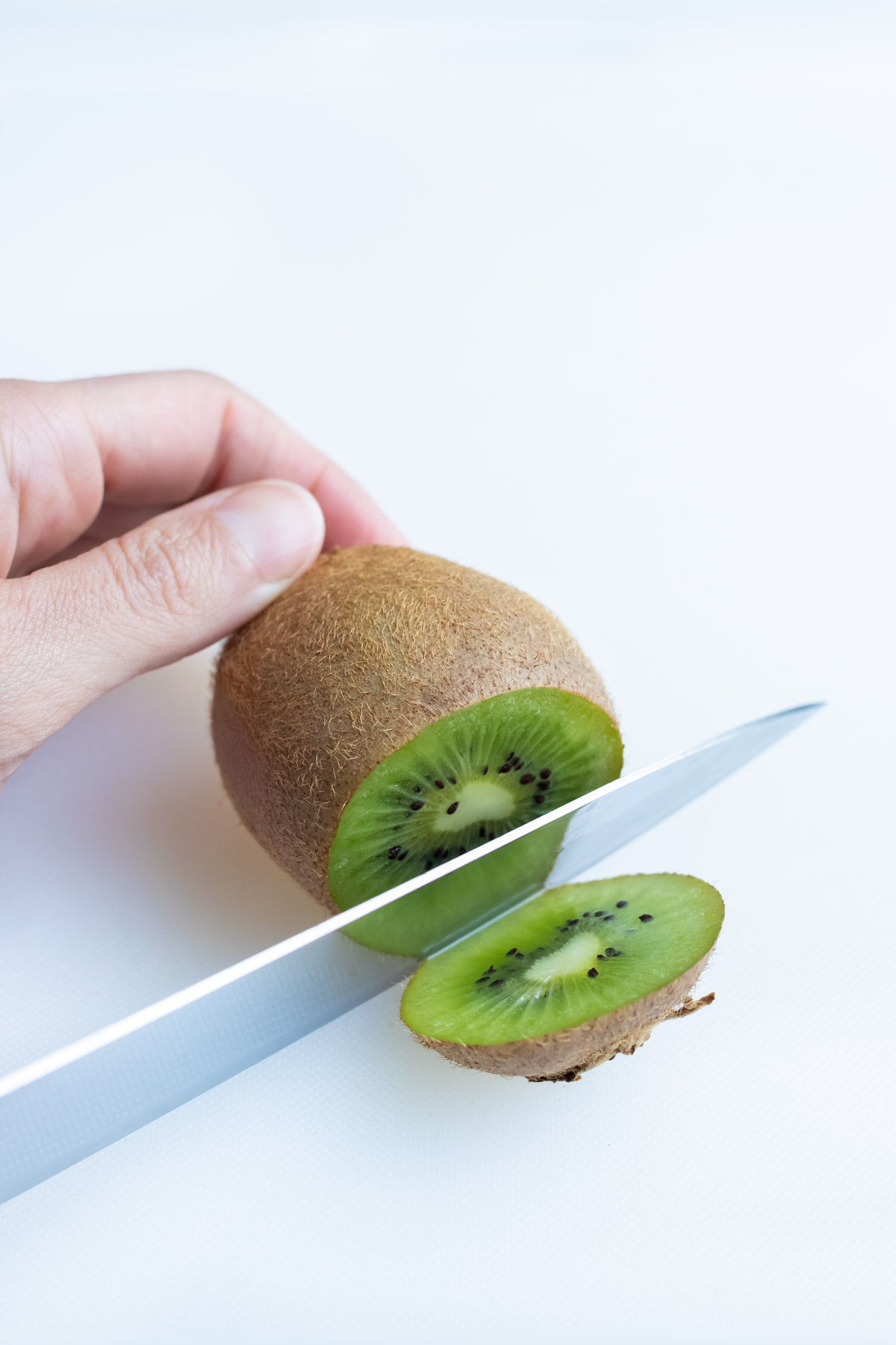 A long knife is used to cut off the end of one kiwi.