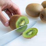 A kiwi is cut with a knife on the counter before removing from the skin.