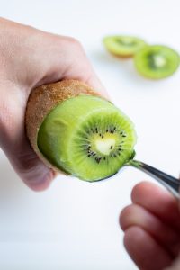 A metal spoon is used to remove the kiwi fruit from the skin.