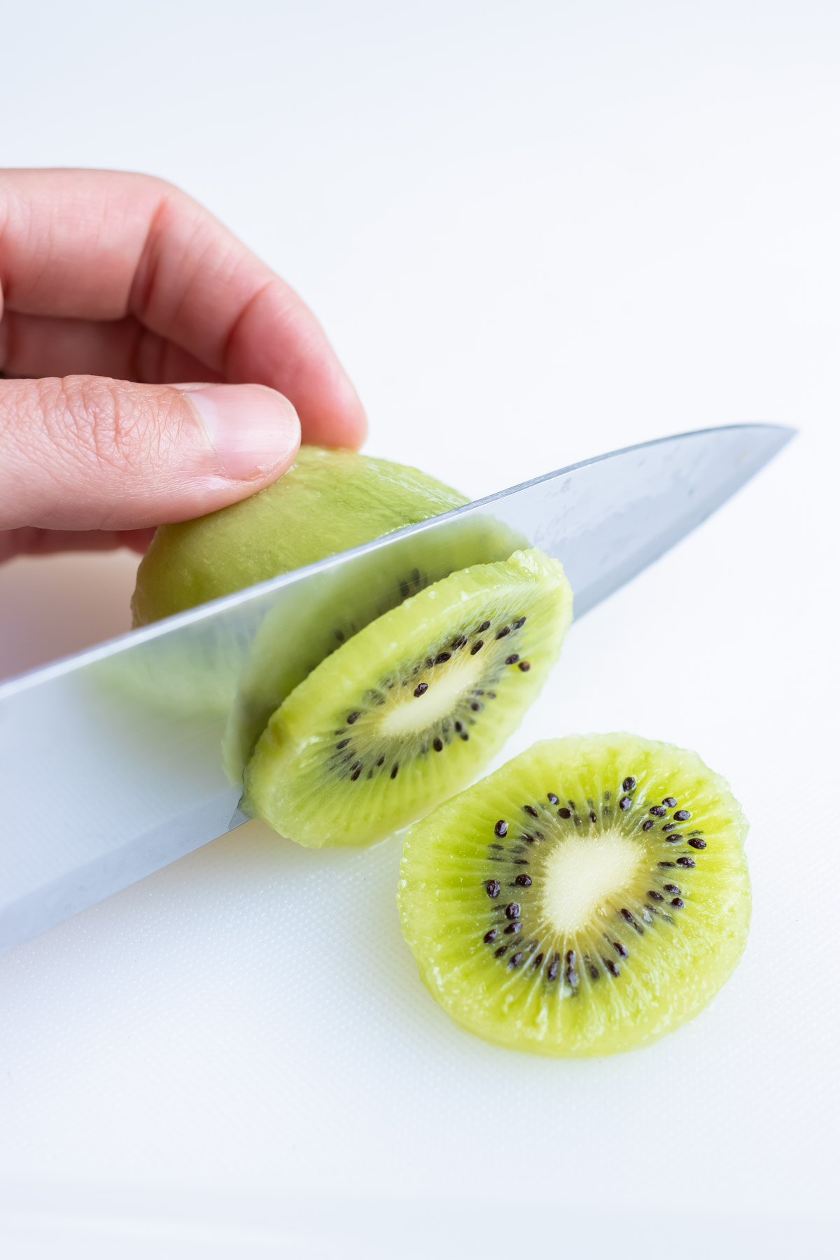 A knife is used to create slices of kiwi.