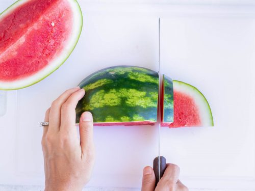 Slicing half a watermelon with the outside on.