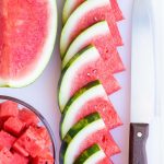 Watermelon wedges in a row on a cutting board next to a knife.