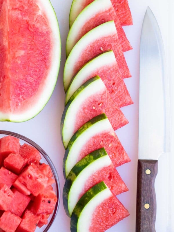 Watermelon wedges in a row on a cutting board next to a knife.