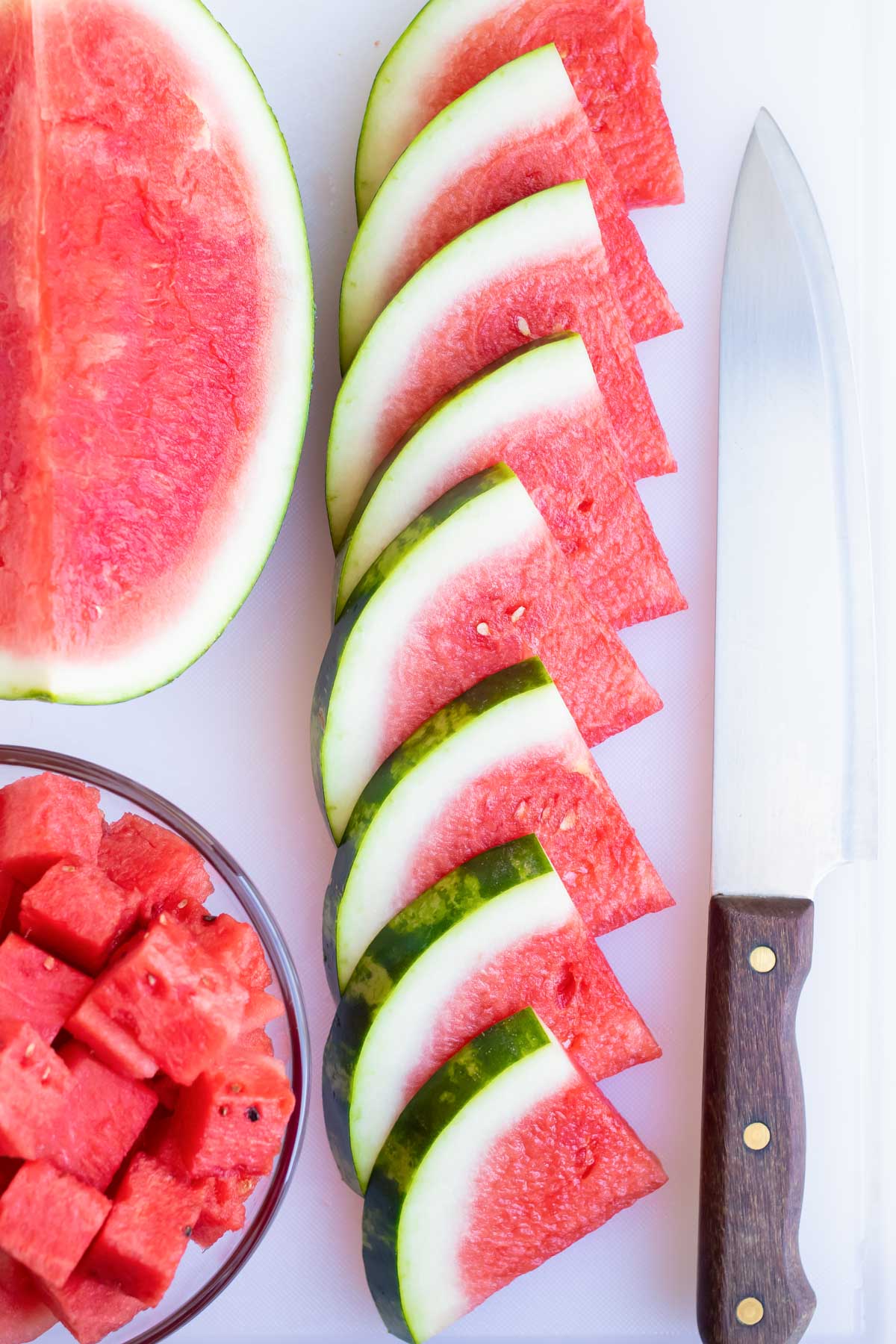 Watermelon wedges in a row on a cutting board next to a knife.
