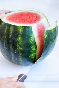 Carefully slicing the peel off of a watermelon.