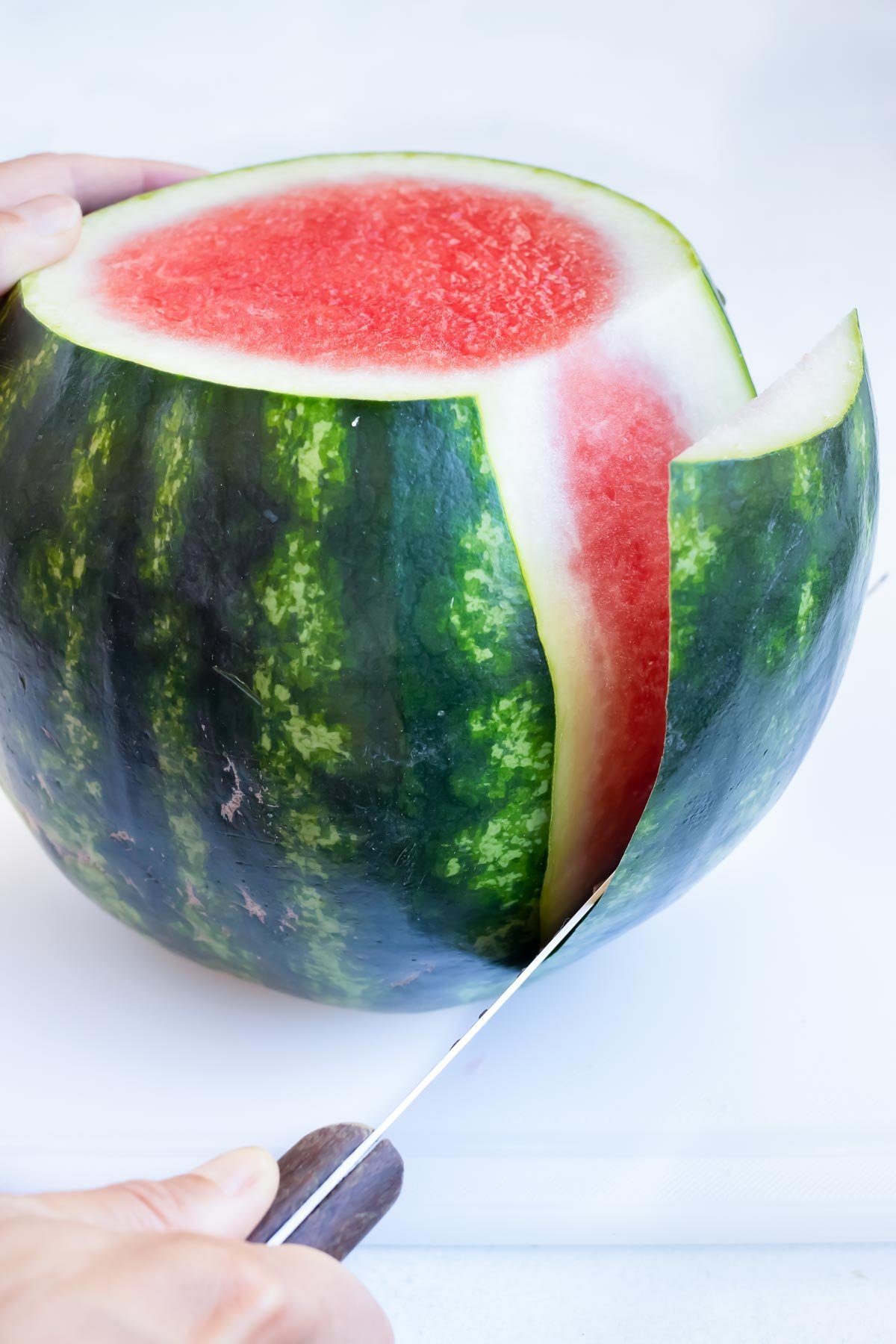 Carefully slicing the peel off of a watermelon.