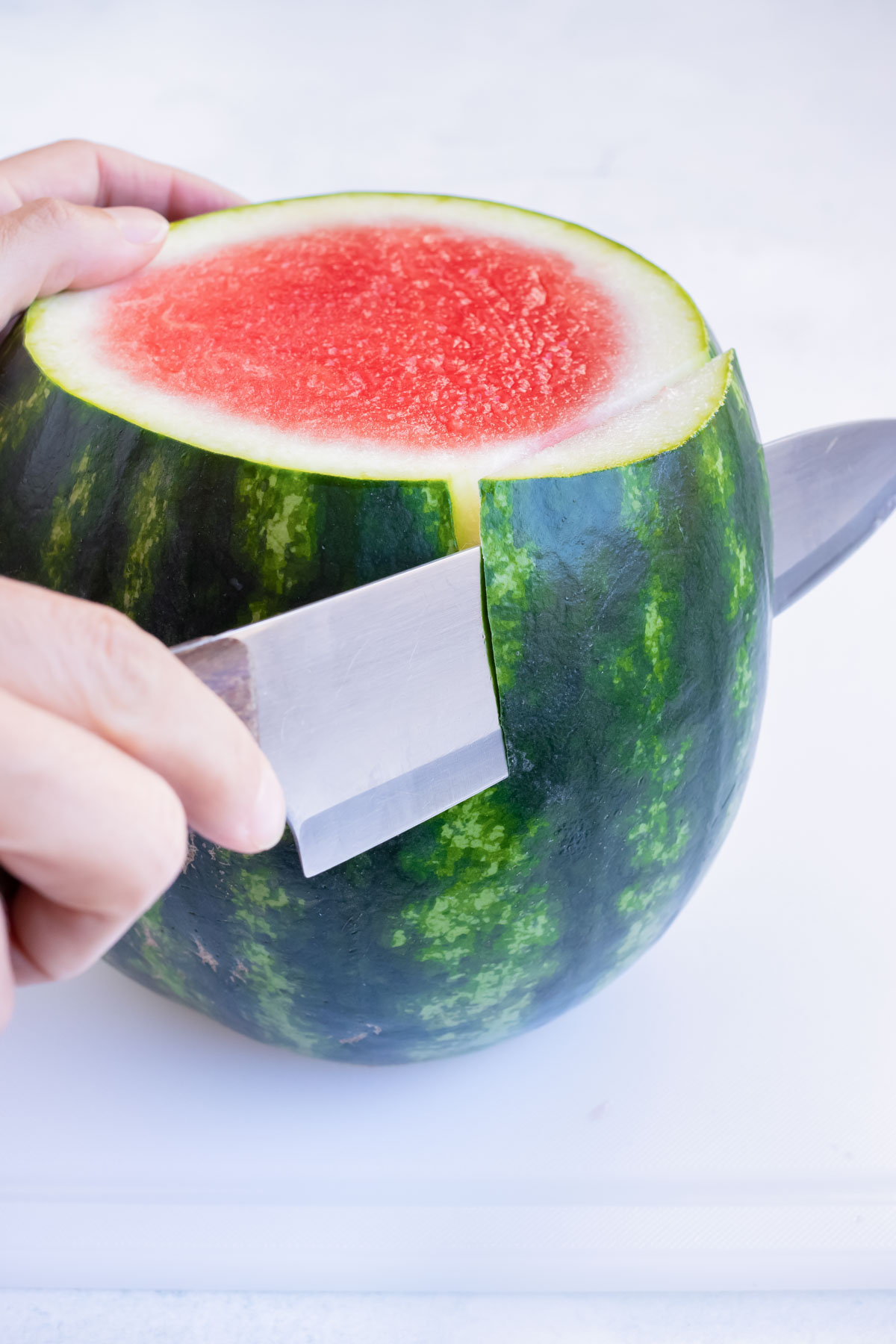 A sharp knife removing the green rind of a watermelon