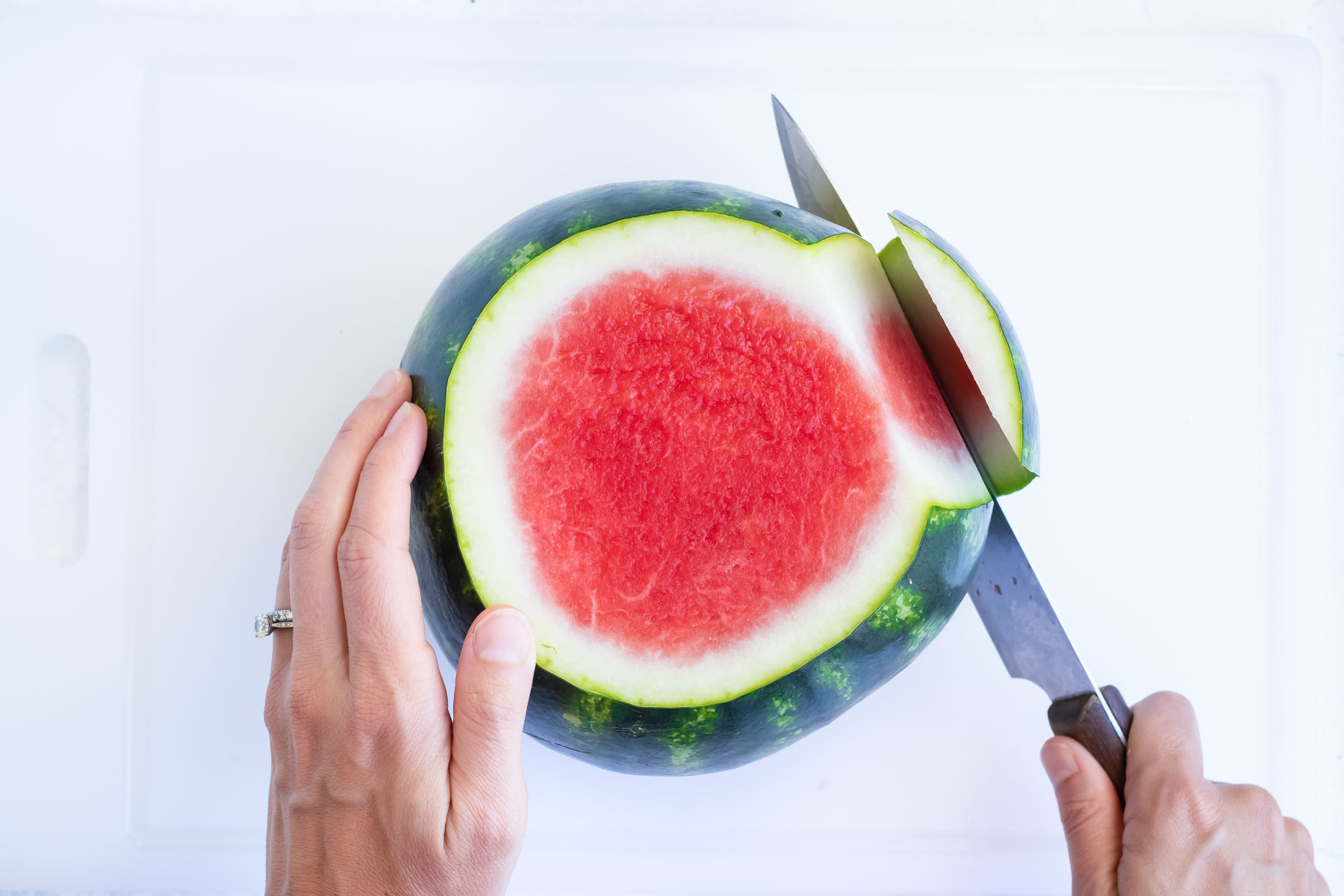 A top view of a knife removing the rind from a watermelon.