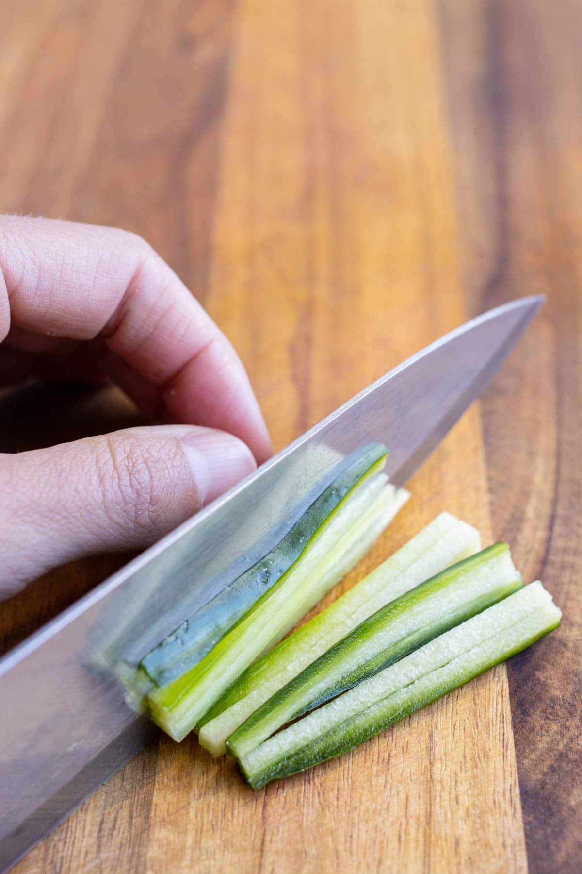 Stacked cucumber planks are cut into Julienne strips.