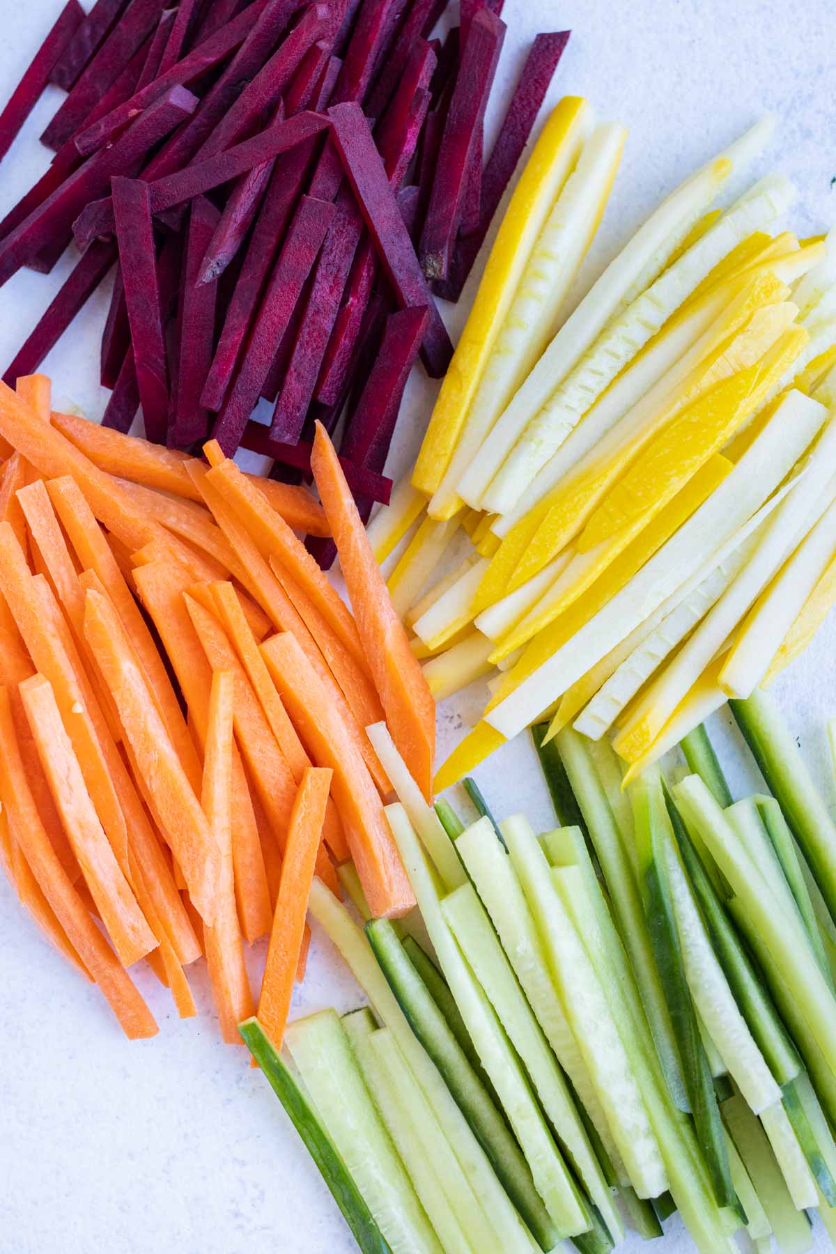 All of the Julienne cut vegetables are shown on the counter next to each other.