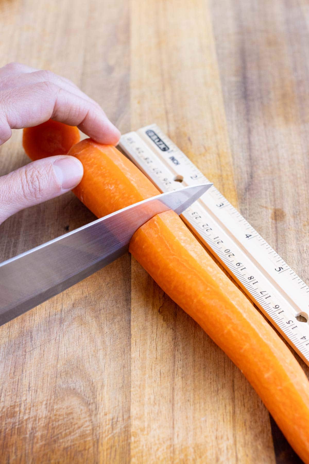 The peeled carrot is measured and cut into smaller sections.