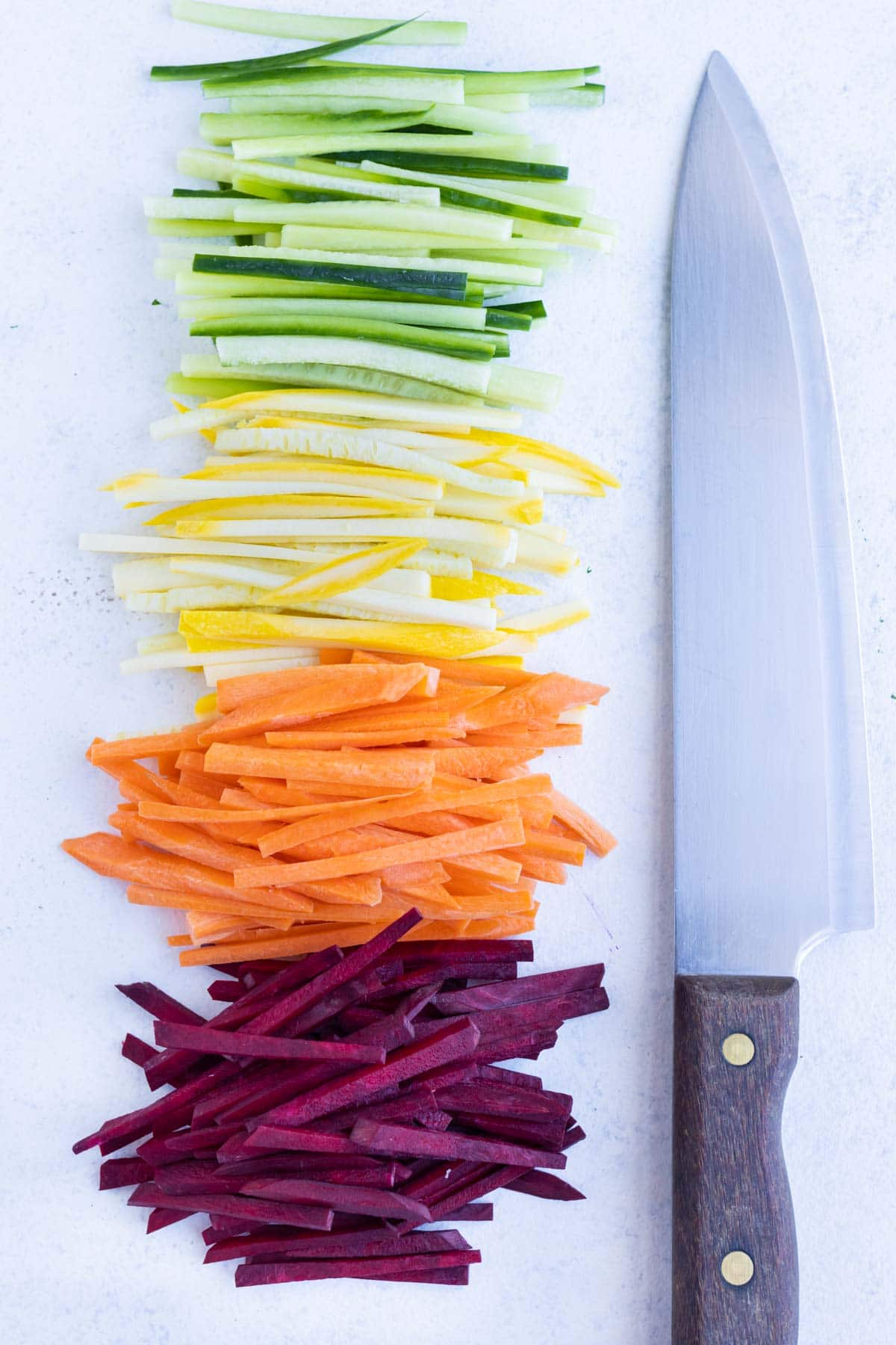 A knife is set next to a pile of Julienne vegetables.