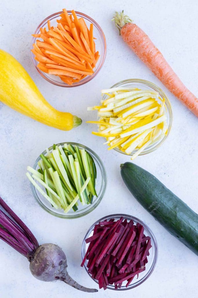 Julienne vegetables are shown in bowls on the counter.