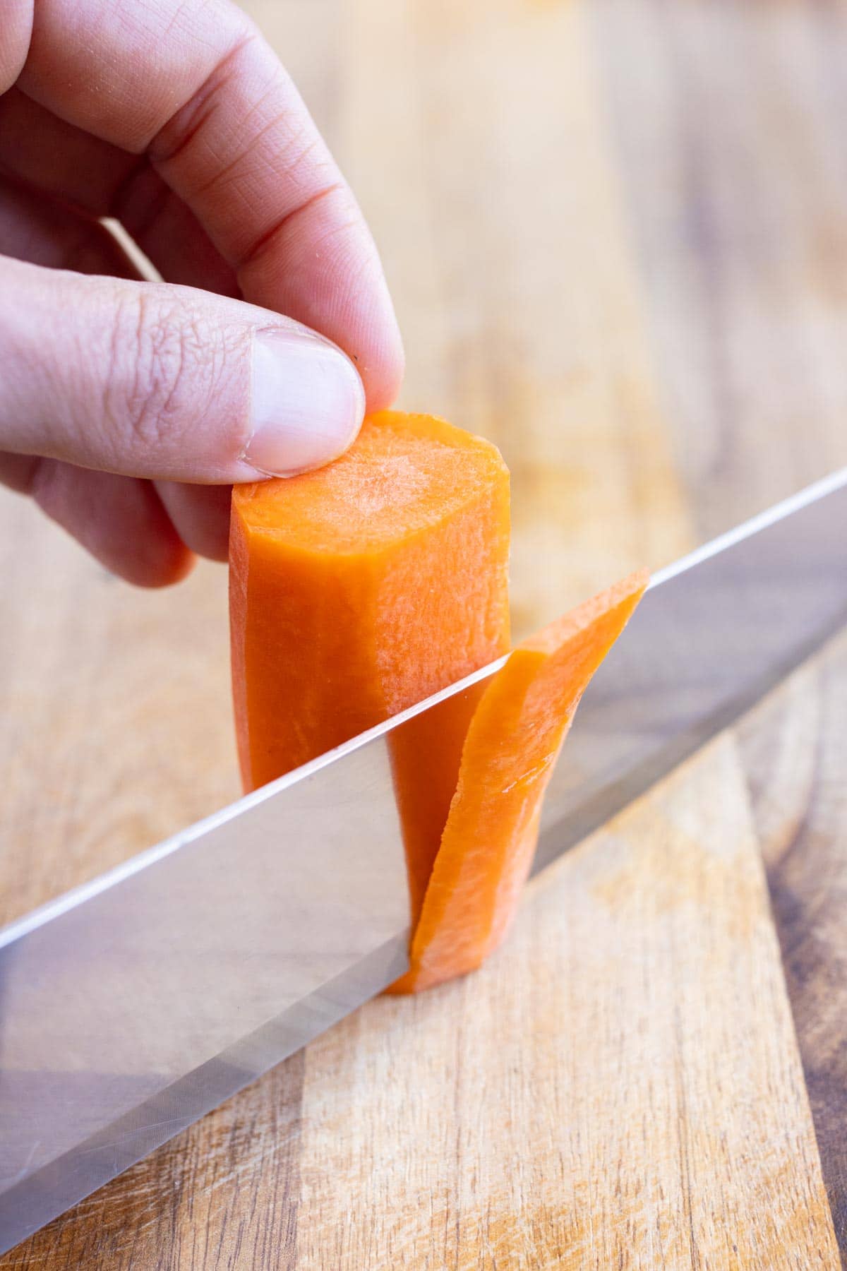A knife is used to cut the carrot into thin strips on a cutting board.