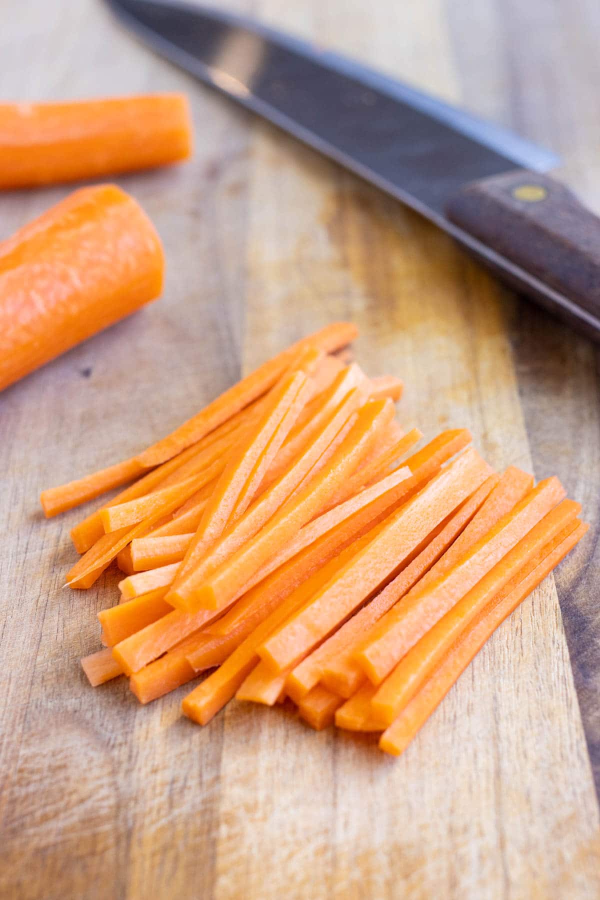 A pile of julienne strips of carrots are shown on the cutting board.