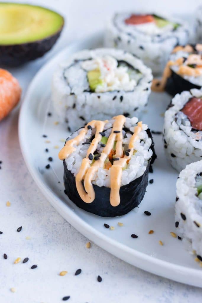 Homemade sushi rolls are topped with sriracha and served for dinner.