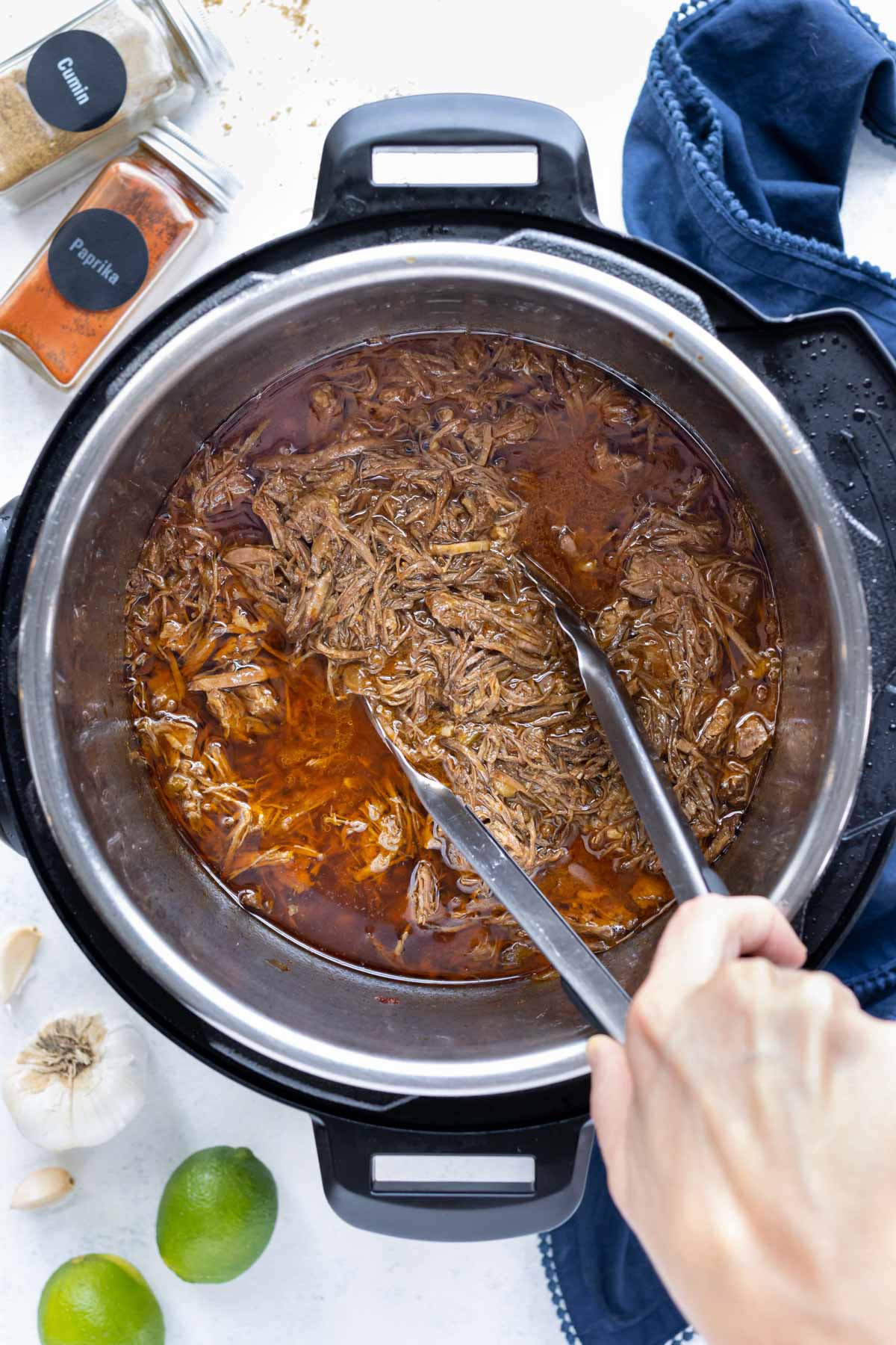 Tongs are used to mix the tender Mexican beef into the sauce.