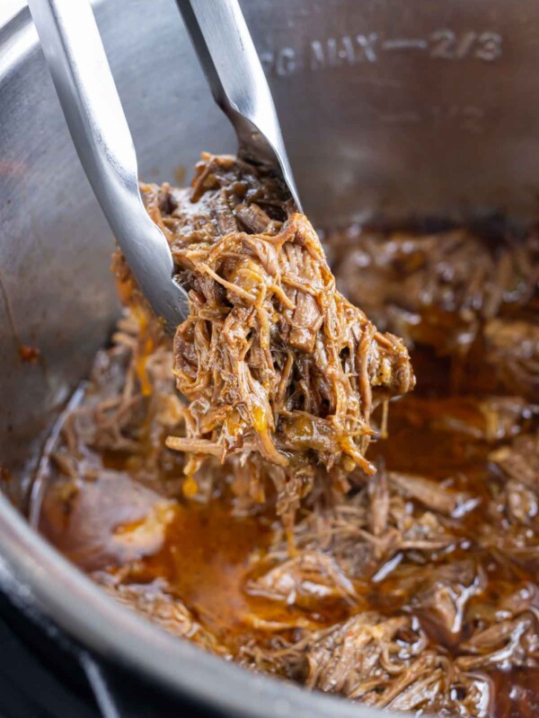 Shredded Mexican beef is removed from the pressure cooker with tongs.